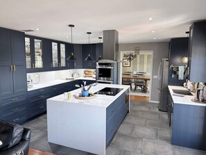 Una cucina moderna con mobili scuri, un'isola centrale e un'area pranzo con un lampadario.