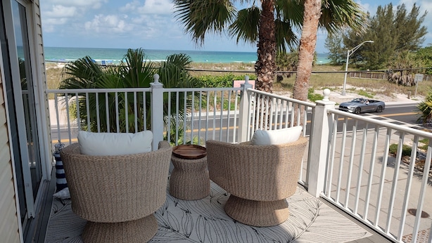A balcony with wicker furniture, a small table, and a view of the ocean.