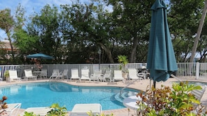 A swimming pool with white lounge chairs and a green umbrella.