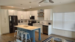 A modern kitchen with white cabinets, a stainless steel refrigerator, a blue island with stools, and a window with blinds.
