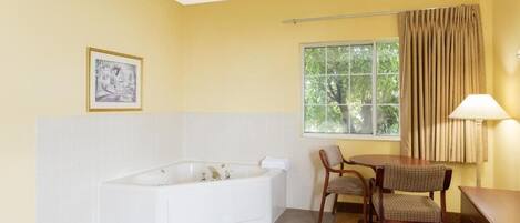 Un baño con bañera, ventana con cortinas, una silla y una mesa.
