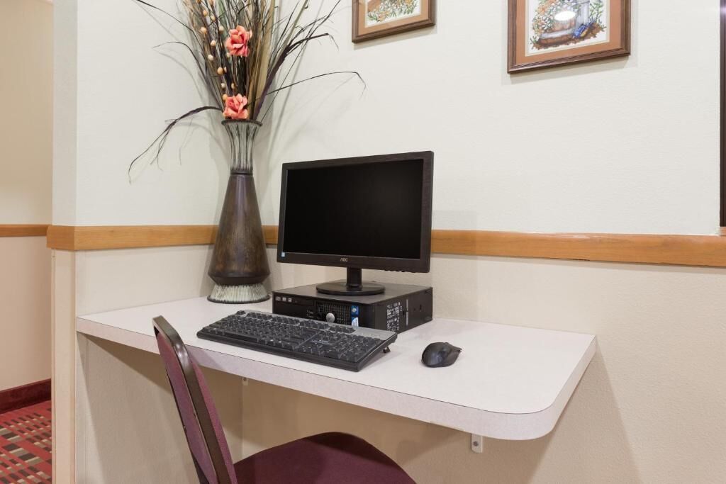Un bureau équipé d’un ordinateur, comprenant un écran, un clavier et une souris. On peut y voir un vase contenant des plantes et des fleurs séchées.
