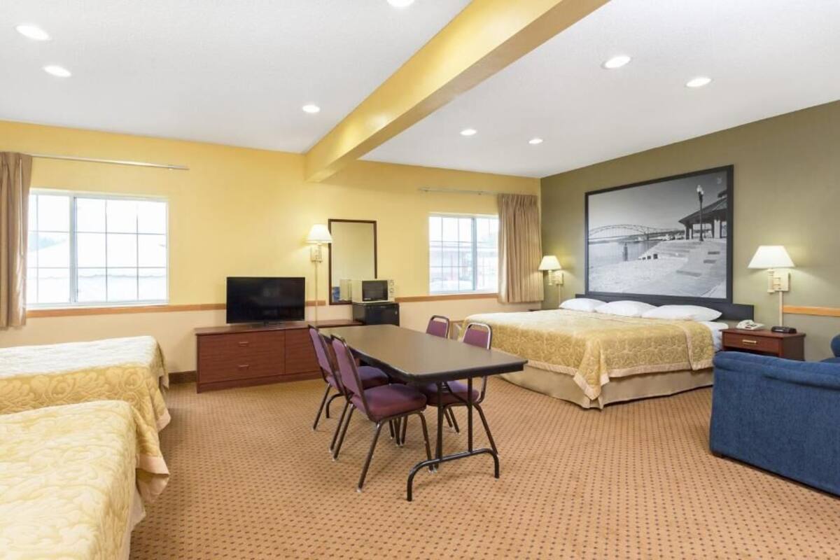A hotel room with two beds, a dining table, chairs, a TV, and a large window.
