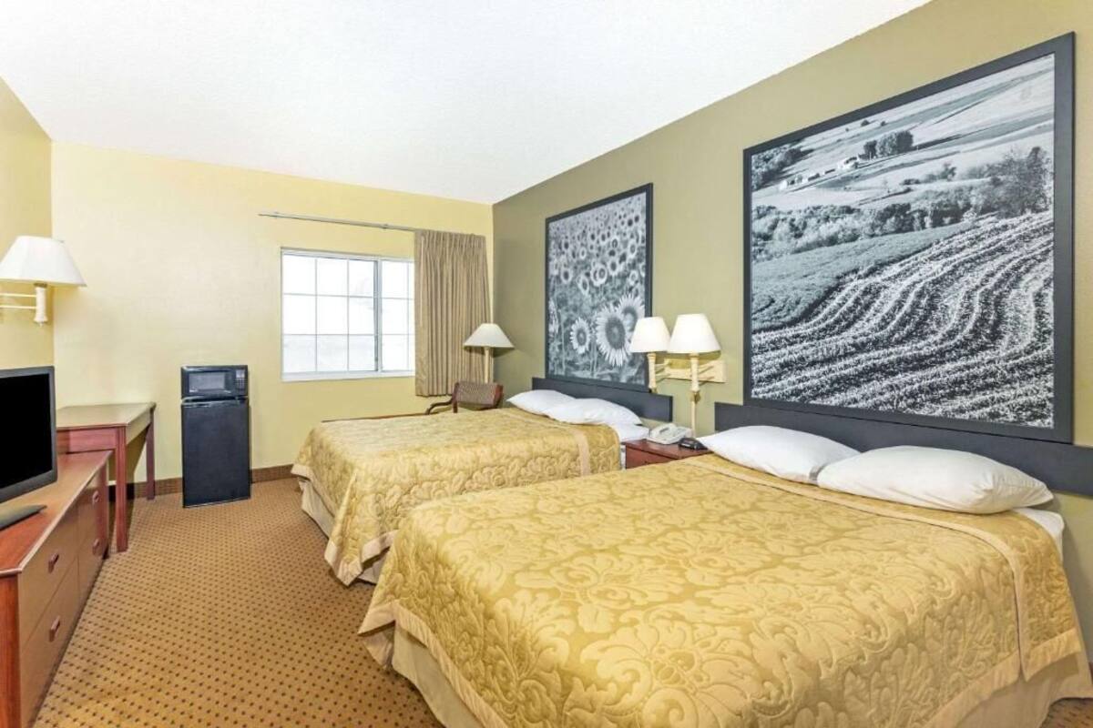 A hotel room with two beds, a desk with a television, a refrigerator, and two lamps.