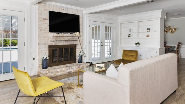 Una sala de estar con chimenea, un sofá, un sill ón amarillo y un televisor montado en la pared.