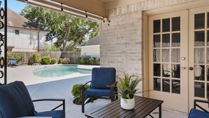 Un área de patio techada con piscina, mobiliario exterior y una pared de ladrillo.