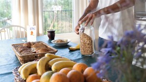 Una persona amb una samarreta blanca abocant grans d'un brossat a un plat. Hi ha cistells amb fruita i un ram de flors damunt la taula.