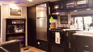 A compact kitchen with a refrigerator, stove, microwave, and a coffee machine.