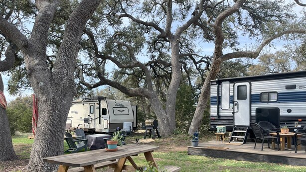 A campsite with a large RV, picnic tables, and outdoor seating.