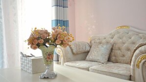 Un sofá elegante y mullido con diseño capitonado, un jarrón decorativo con flores y un dispensador de pañuelos sobre una superficie blanca.
