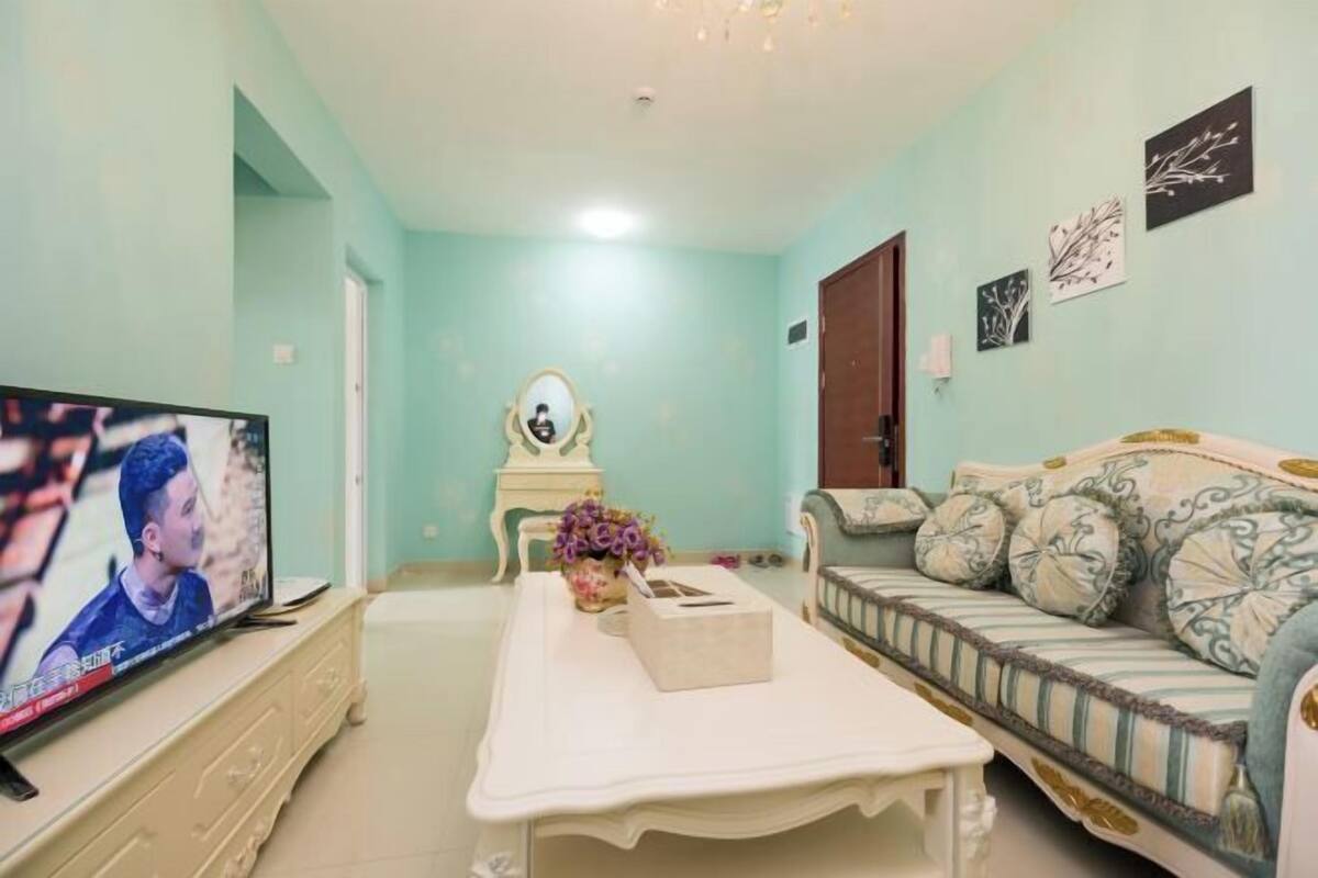 A living room with a television, a sofa, a coffee table, and a mirror.