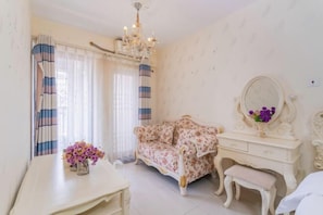 Una habitación con sofá floral, tocador con espejo y candelabro.