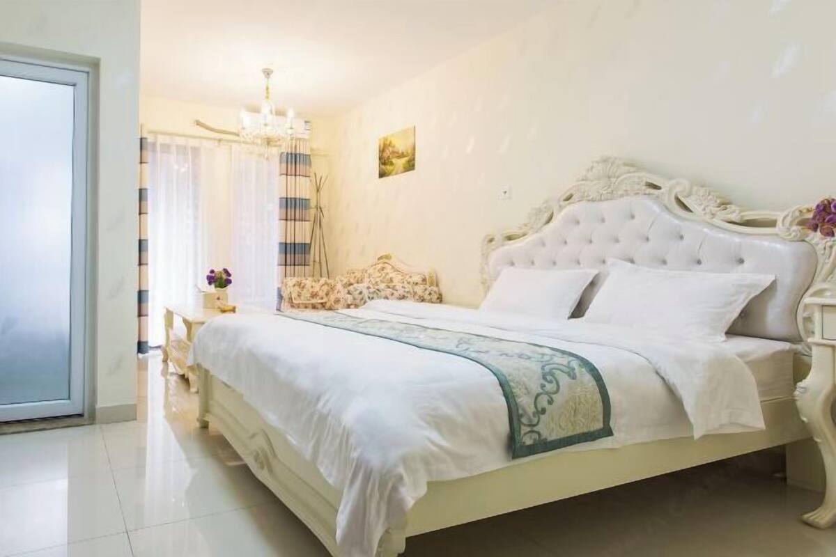 A neatly made bed with a white and green bedspread, a chandelier, and a painting on the wall.