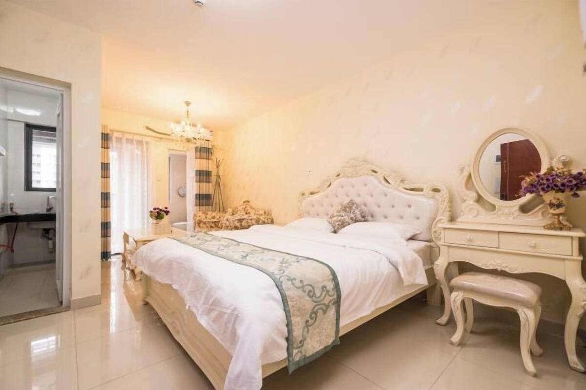 A bedroom with a large bed, a vanity with a mirror, and a chandelier.