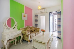 Una habitación con pared verde y rosa, un sofá floral, un tocador blanco con espejo y una mesa blanca con un jarrón de flores.