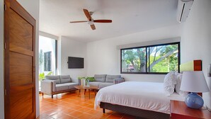 A modern hotel room with a large bed, two sofas, a small table, and a ceiling fan.