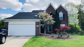 A two-story house with a garage, a well-maintained lawn, and flowering plants.
