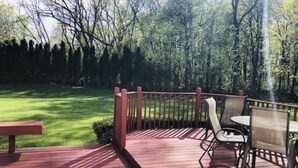 A wooden deck with a table and chairs, surrounded by a wooden railing and a grassy lawn.