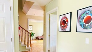 A hallway with wooden flooring, a staircase with a white railing, and two framed artworks on the wall.
