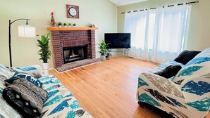 A living room with a brick fireplace, a flat-screen TV, and two patterned sofas.