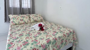 Un lit simple avec une literie à motifs floraux, une serviette enroulée et une fleur rouge posée sur le lit.