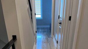 A hallway with wooden flooring, a staircase with a black railing, and a window with blinds. - Center City Philadelphia rooftop (Philadelphia)