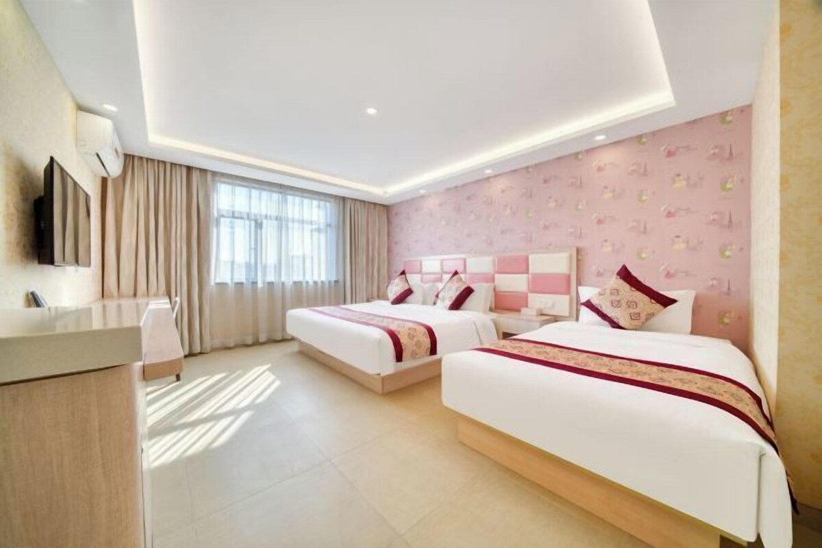 A hotel room with two beds, a desk, and a large window with curtains.