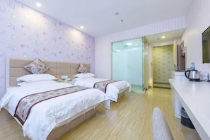 Ein Hotelzimmer mit zwei Betten, Holzboden, weißer Wand mit dezentem Muster und einer kleinen Küchenzeile.