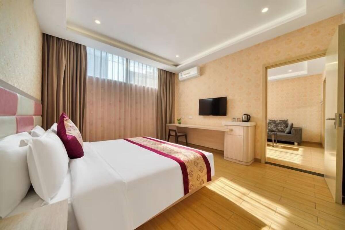 A hotel room with a bed, desk, chair, television, and a view into another room.
