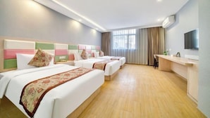 Ein Hotelzimmer mit drei Betten, einem Schreibtisch und einem Fernseher.