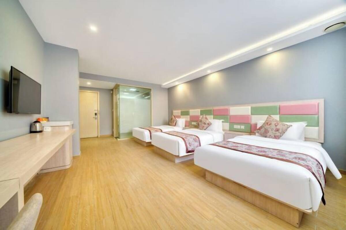 A hotel room with two beds, a desk, a flat-screen TV, and a door leading to another room.