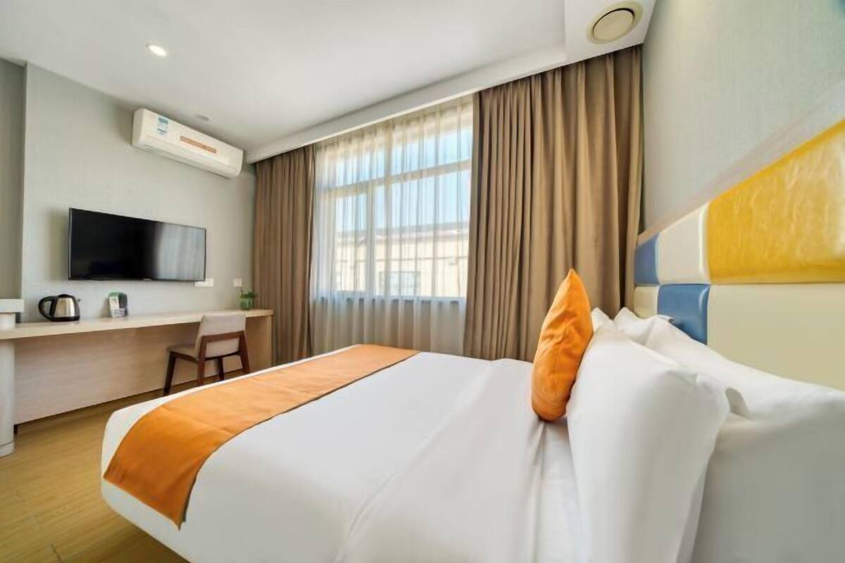 A hotel room with a bed, a desk, a television, and a window with curtains.