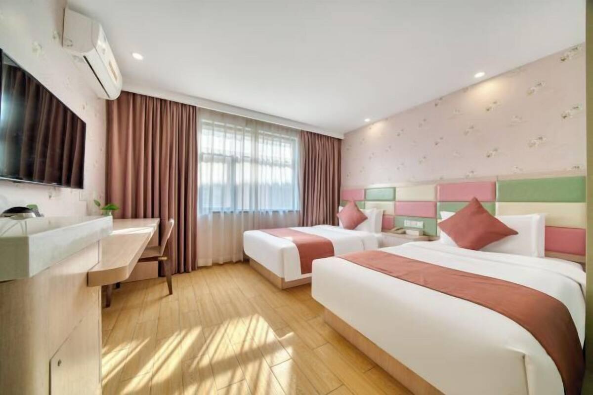 A hotel room with two beds, a TV, a desk, and a window with curtains.