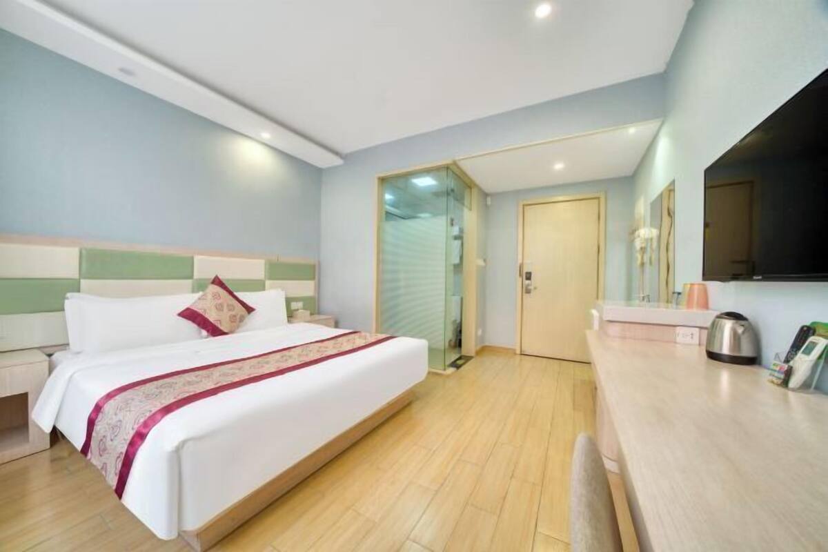 A hotel room with a bed, bedside table, and a small kitchenette area.