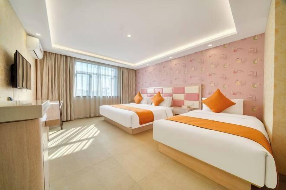 A hotel room with two beds, a desk, and a large window.