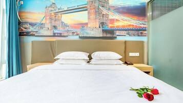 Ein Hotelzimmer mit Bett, Kissen, einem Nachttisch, einer Wand mit einem Wandgemälde einer Brücke und einem Fenster mit Vorhängen.