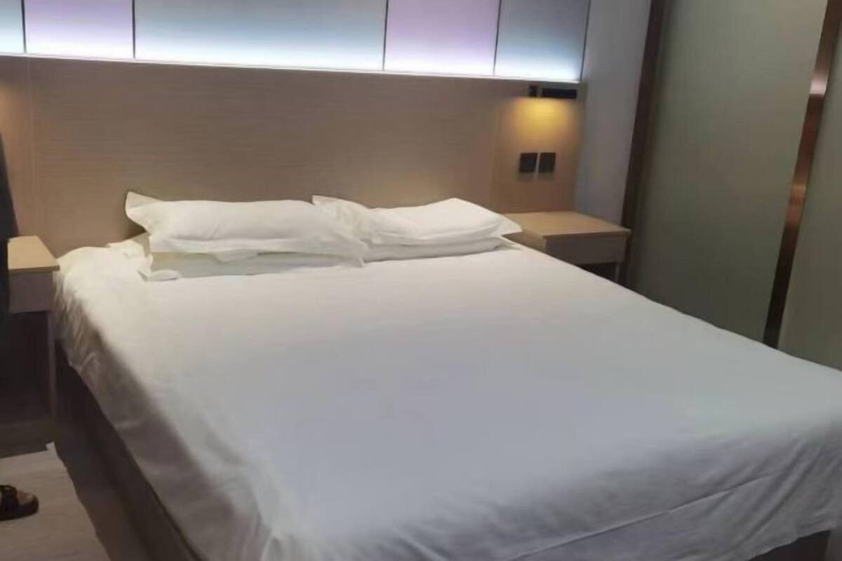 Una cama bien tendida en una habitación de hotel moderna, con cabecera, mesitas de noche y una lámpara de pared.