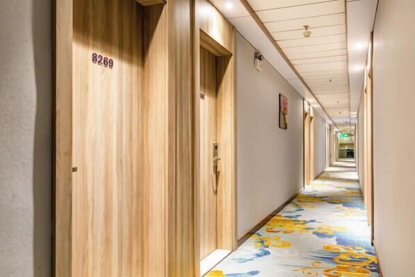 Ein Hotelgang mit Holztüren, die mit 8269 nummeriert sind, einem blumigen Teppich und einem geraden Korridor, der zu einem hellen Raum am Ende führt.