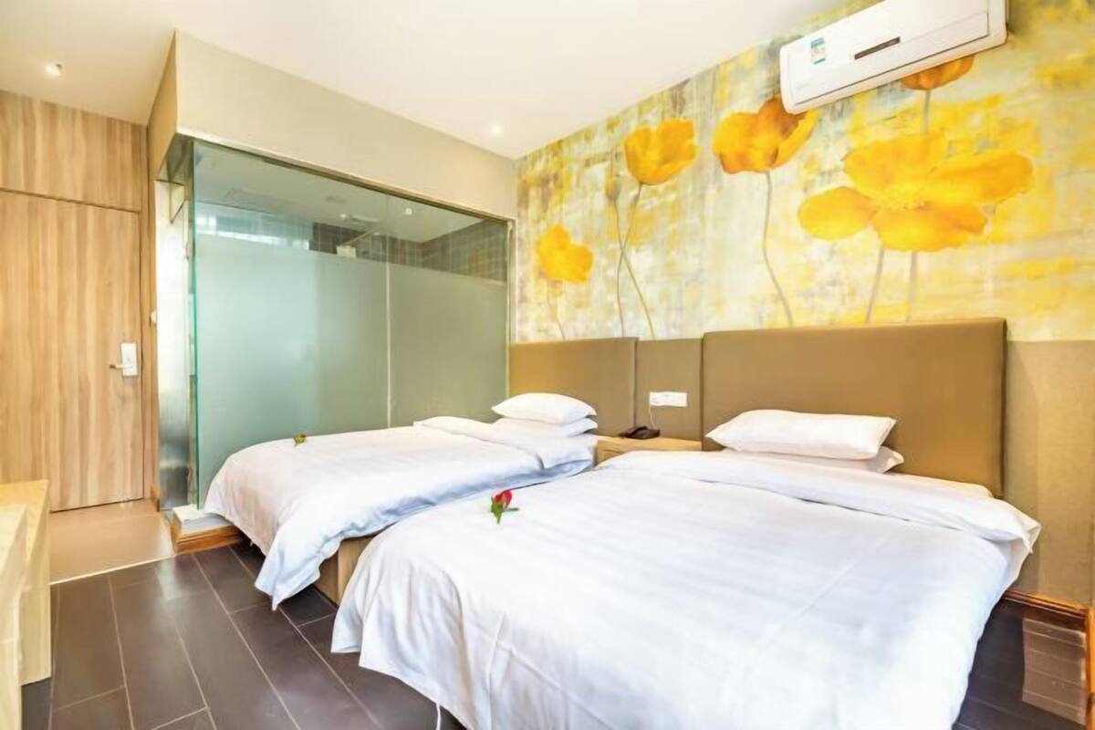 Habitación de hotel con dos camas, cabina de ducha de vidrio y una pared con un mural floral.