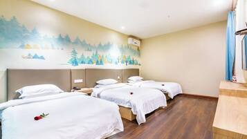 Habitación de hotel con cuatro camas individuales, suelo de madera, un mural en la pared y un pequeño escritorio con lámpara.