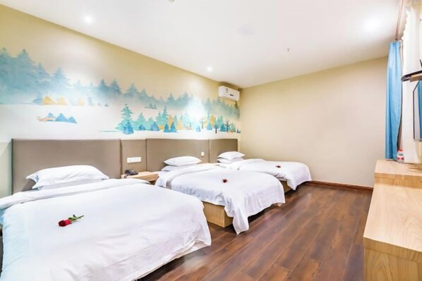 A hotel room with four single beds, a wooden floor, a mural on the wall, and a small desk with a lamp.