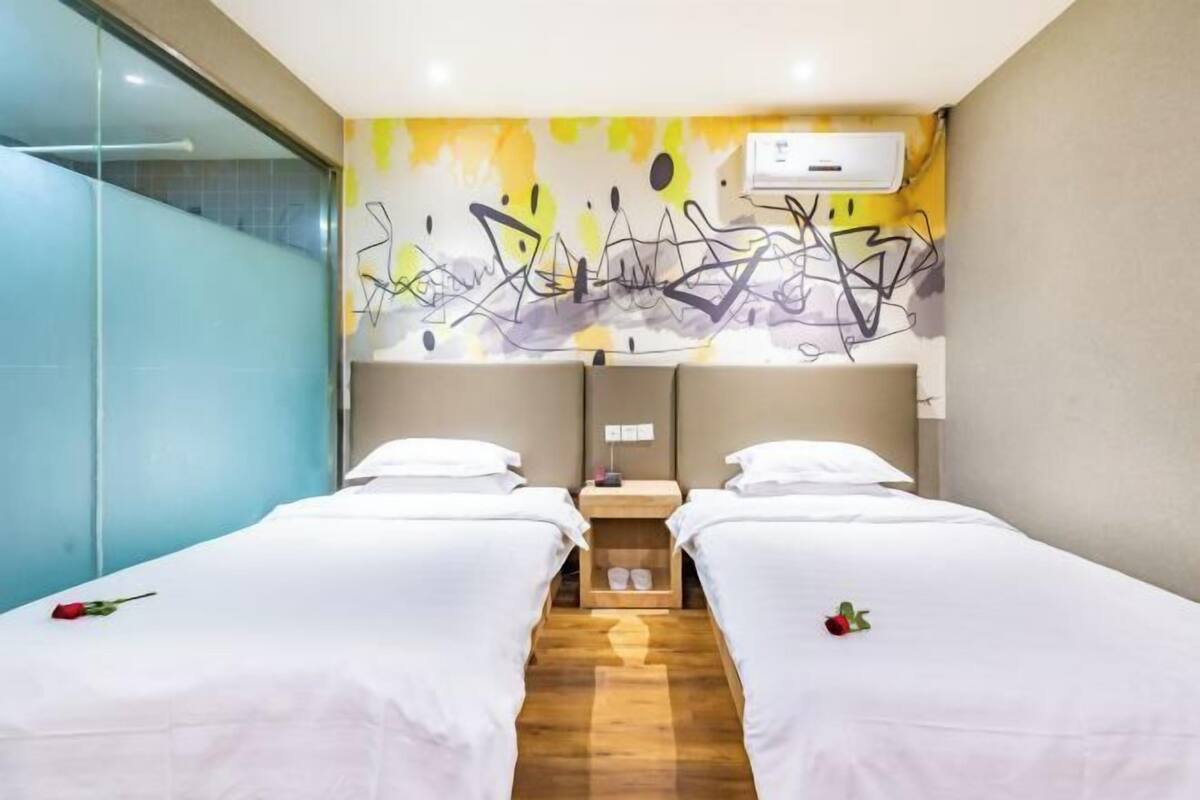 Habitación de hotel con dos camas, piso de madera, una pared con arte abstracto y una ventana.