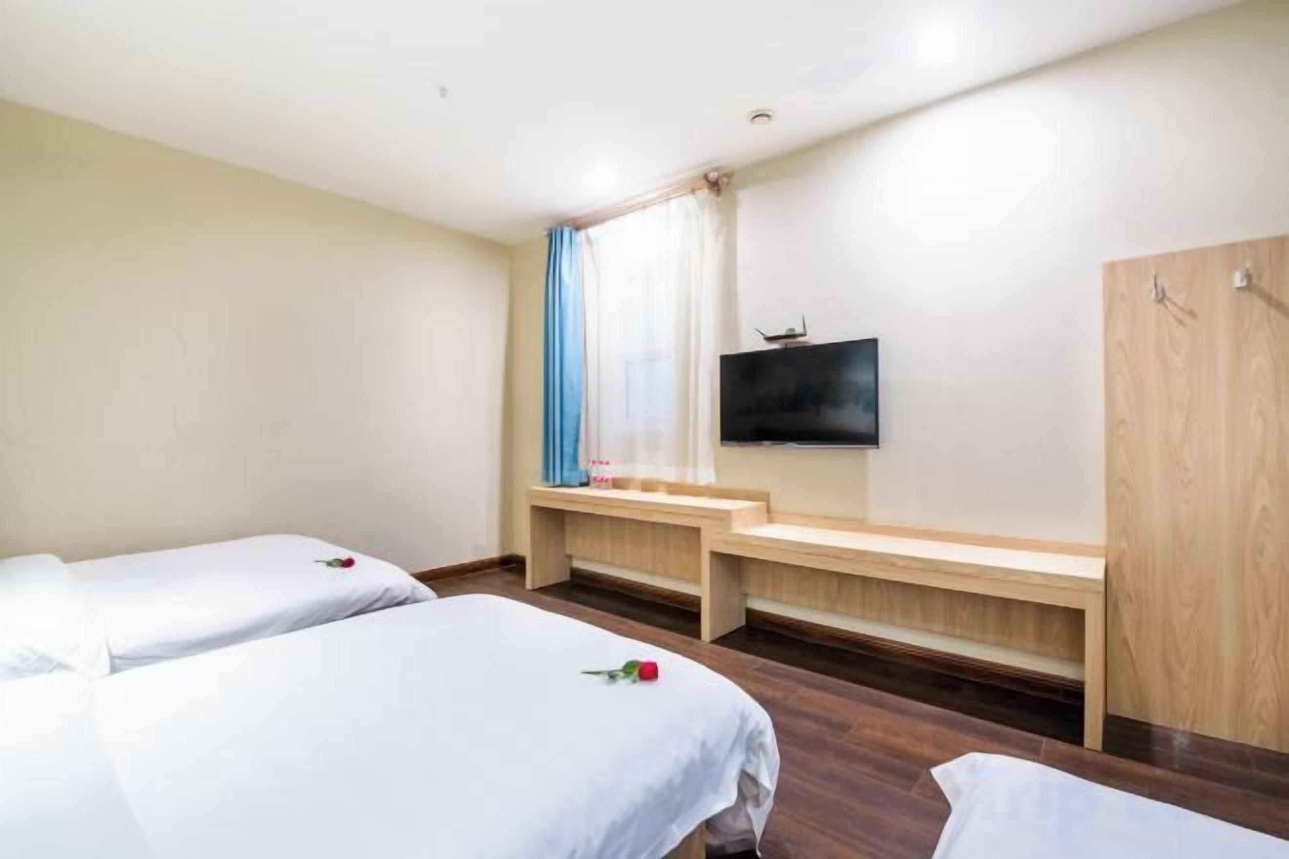 A hotel room with two beds, a TV, a wooden bench, and a wardrobe.
