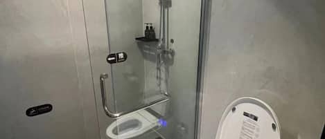 A glass-enclosed shower stall with a handheld showerhead and a toilet with a digital display.