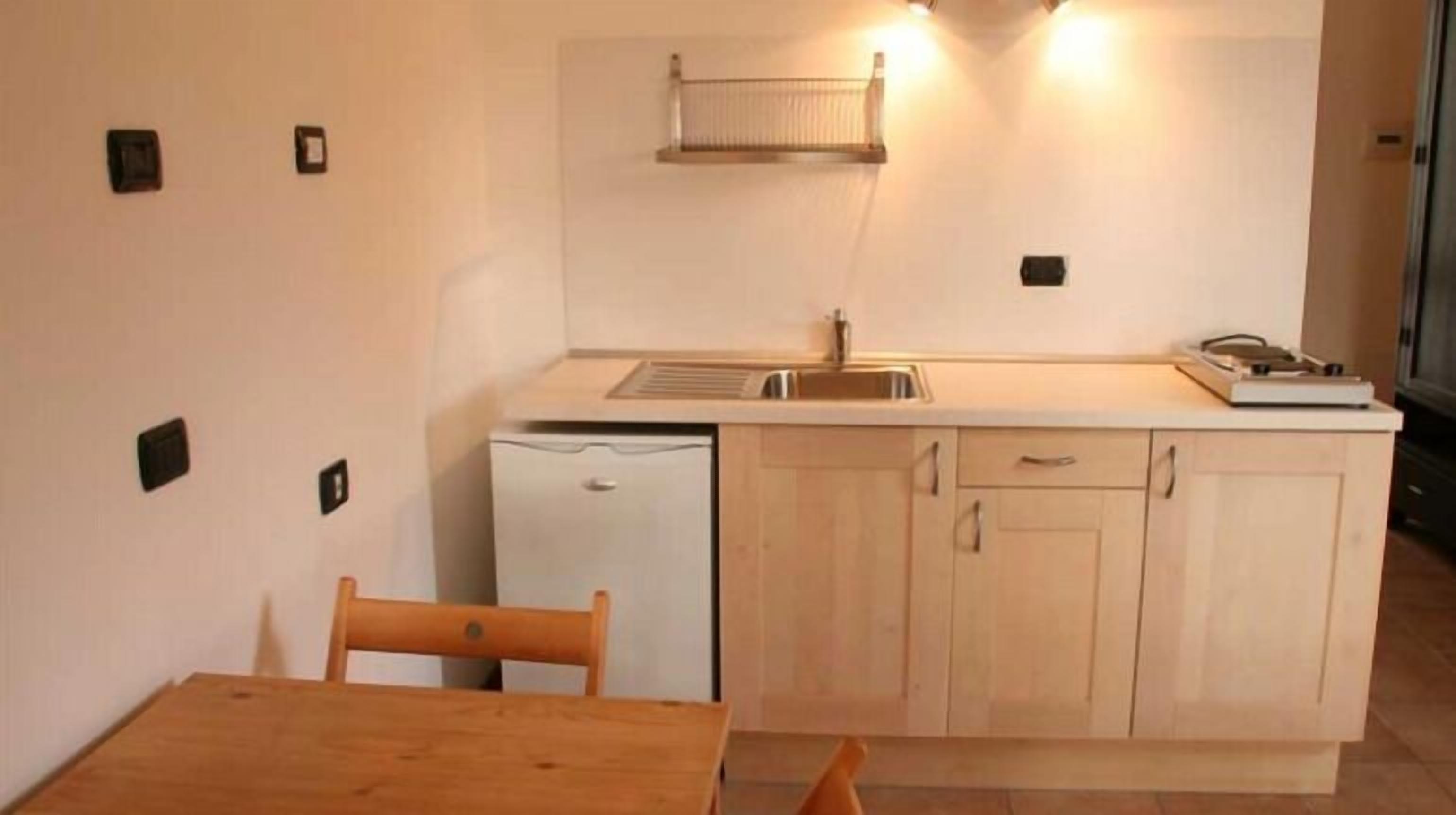 Une cuisine compacte comprenant un évier, un petit réfrigérateur, des placards en bois et une table avec des chaises.