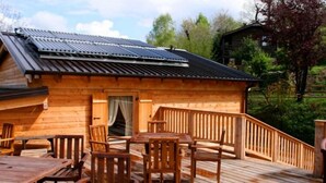 Une cabane en bois dotée d’une terrasse, de panneaux solaires sur le toit et offrant une vue sur le paysage environnant.
