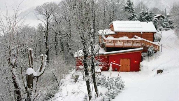 Une cabane en bois à l’extérieur rouge, dotée d’un balcon et entourée d’arbres couverts de neige.
