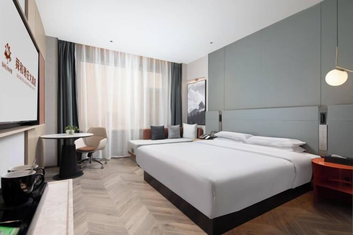 Ein Hotelzimmer mit einem großen Bett, einem kleinen Schreibtisch, einem Sessel, einem Tisch und einem Fernseher.