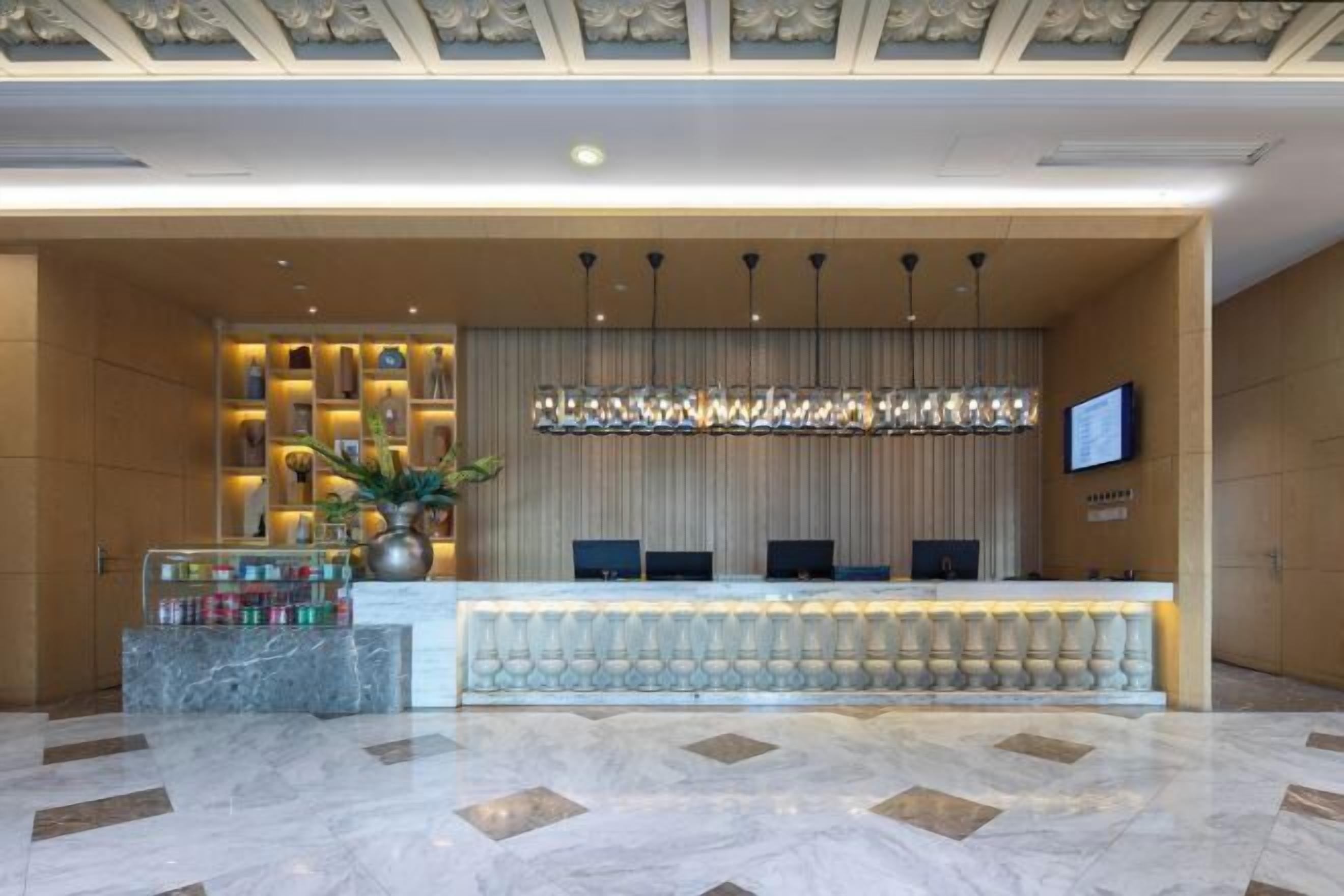 Zona de recepción de un hotel, con suelo de mármol, mostrador de recepción, televisor montado en la pared y techo decorativo.