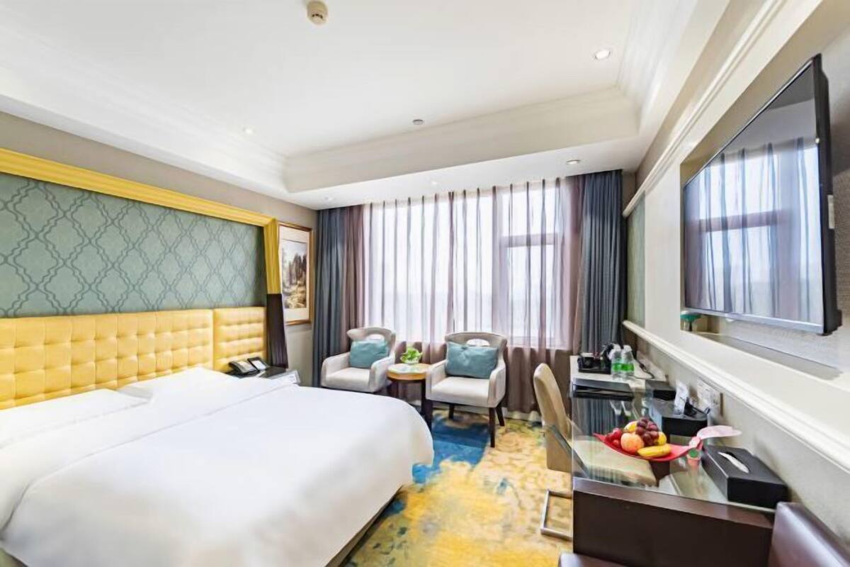Ein Hotelzimmer mit einem großen Bett, zwei Sesseln, einem kleinen Tisch, einem Fernseher und einer Obstschale.